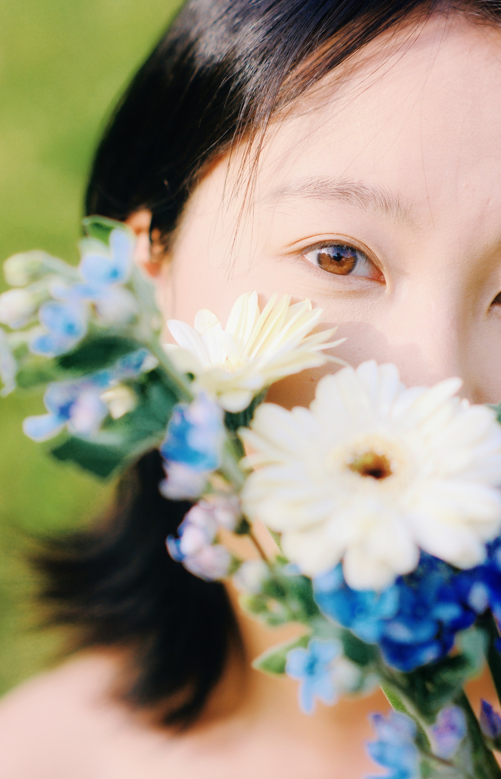 女子在白色和蓝色花朵后露出眼睛